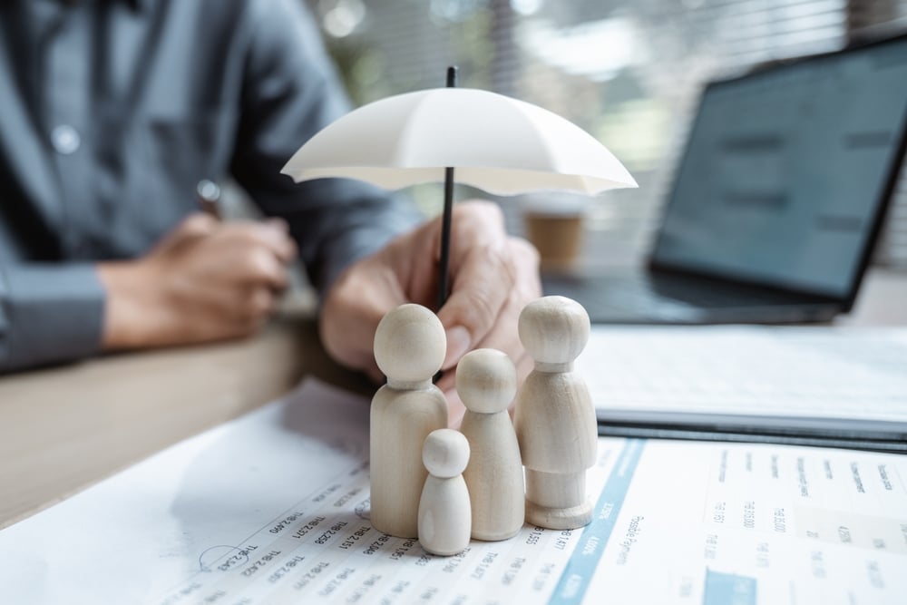 Protection de la famille et assurance vie : nos conseils Figurines de famille protégées par un parapluie sur des documents financiers, illustrant l'assurance vie.